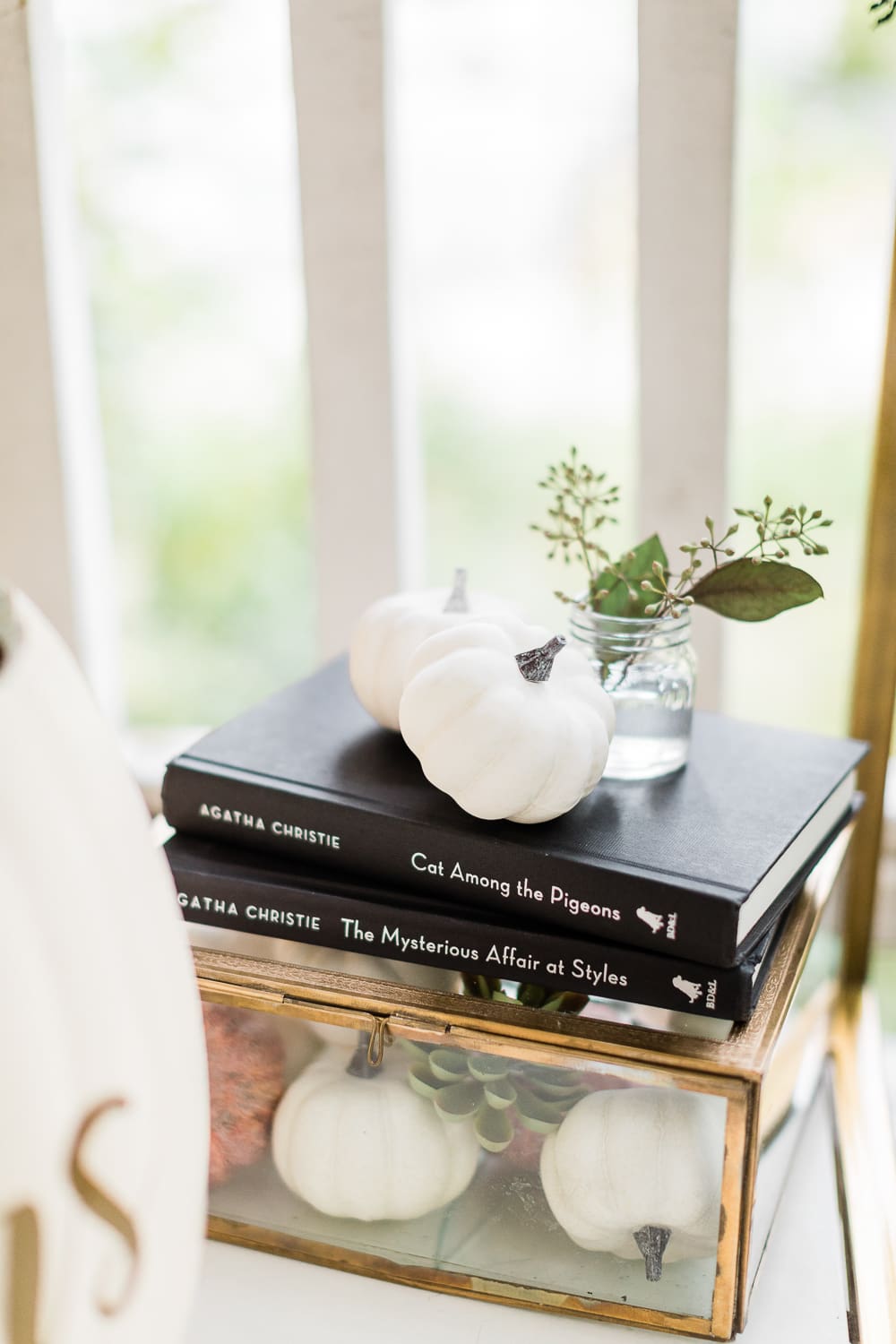 golden glass shadowbox filled with small white pumpkins and succulents, Agatha Christie books on a Halloween bar cart, Halloween Bar Cart + DIY Pumpkin Ice Bucket Tutorial by popular affordable fashion blogger Stephanie Ziajka on Diary of a Debutante, Halloween bar cart ideas, how to decorate a halloween bar cart