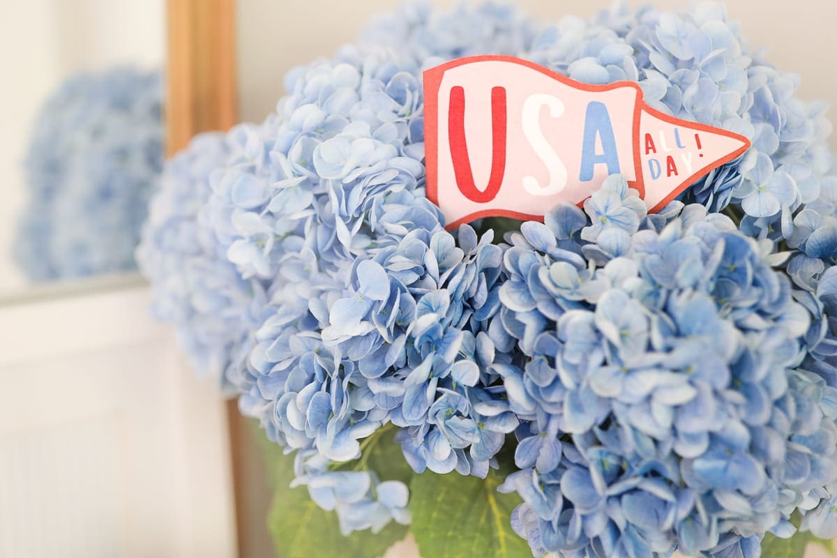 Printable patriotic mini pennant flags tucked into blue hydrangea flower arrangement for a festive 4th of July centerpiece.